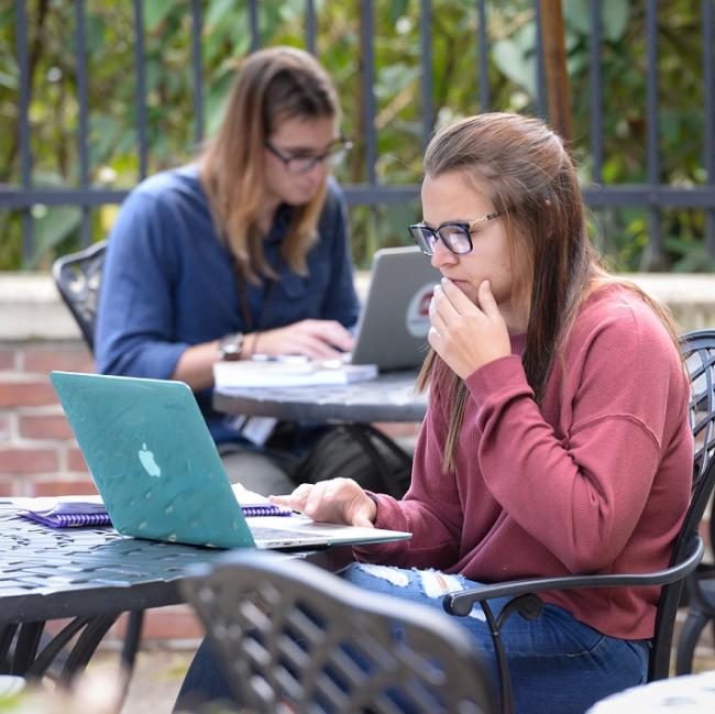 student at computer outside on waynesburg university's campus